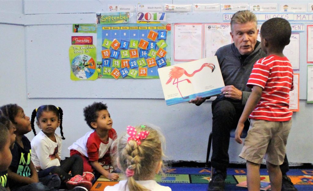 David Cully shows an illustration of a flamingo to a small boy who has stood up to get a closer look, while other pre-schoolers sit on the floor gazing up at them