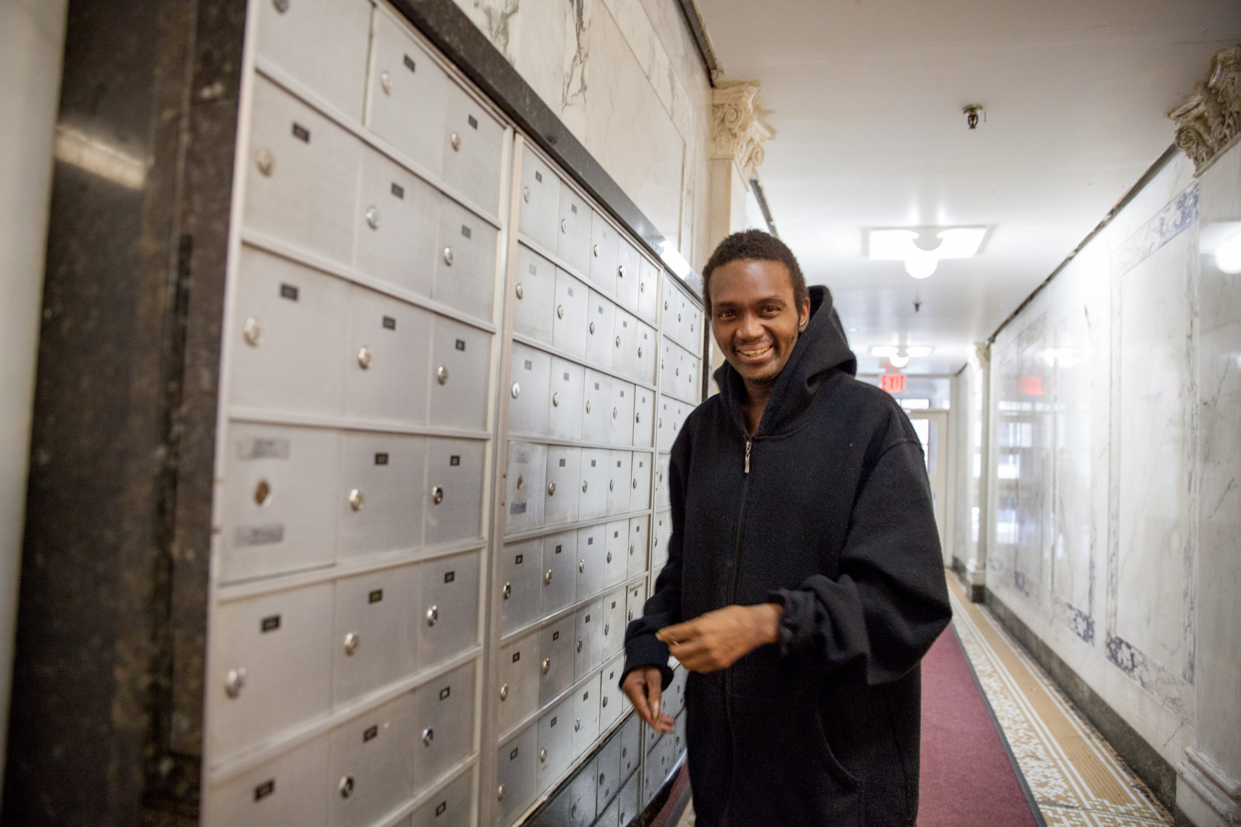 A man standing by a apartment's lobby mailbox area.