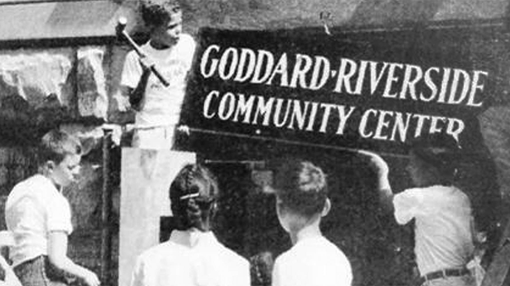 Young people hang a Goddard Riverside sign on a building in an old black and white photo