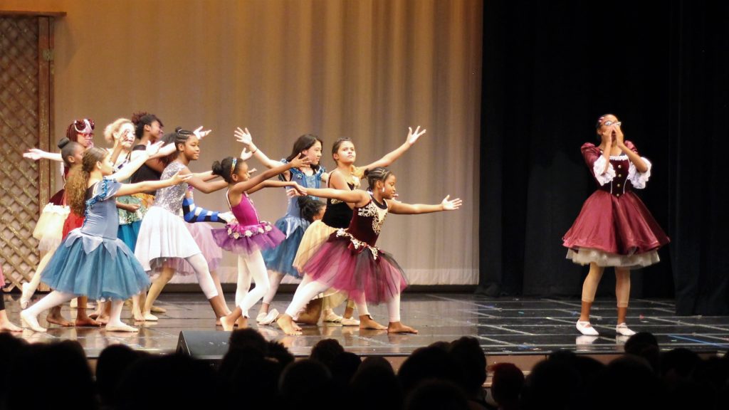 A group of girls with their arms extended towards a young woman with her hands to her face in a shock gesture. During the Performing Arts Conservatory's final performance in 2019.