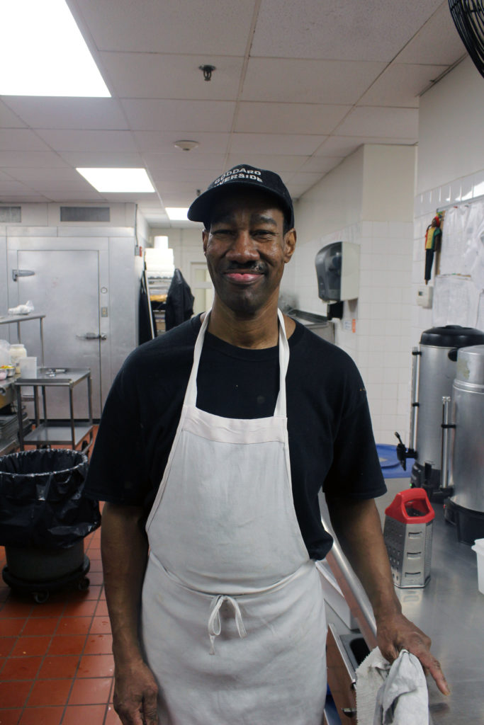 A TOP member works in the Goddard Riverside Senior Center kitchen in a white apron.