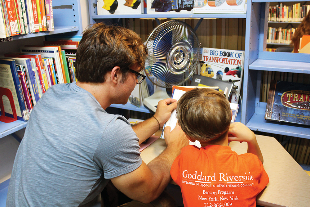 A young man tutoring a young boy at a desk.