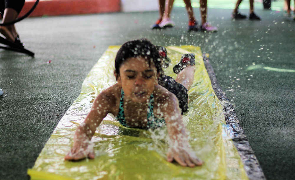 A girl slides headfirst toward the camera on a slip 'n slide at our Lincoln Square Summer Camp