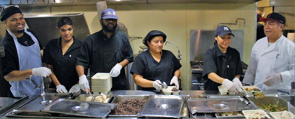 Home Delivered Meals employees stand behind a steam table assembling fresh meals for delivery