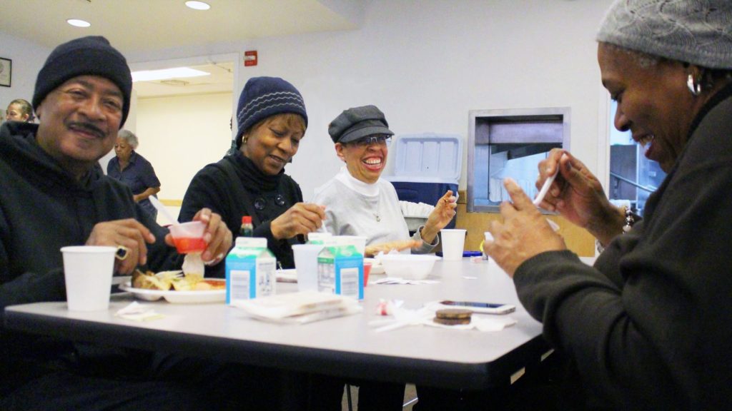 Diverse older adults eat lunch around a table, laughing