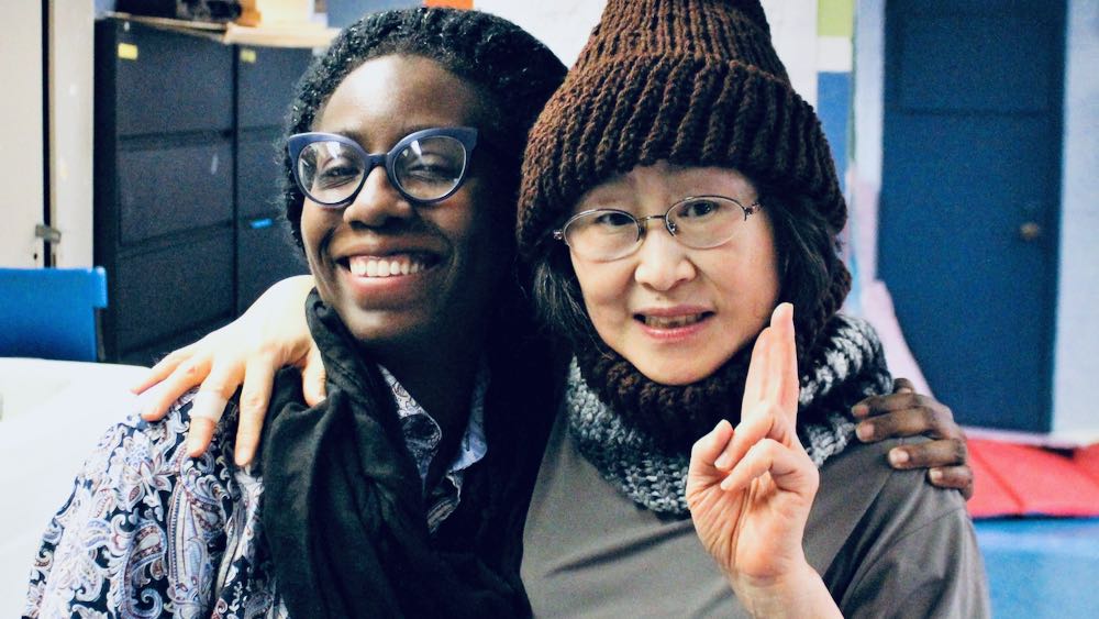 Two women at the Lincoln Square Senior Center drape arms around each others shoulders as one makes the peace sign