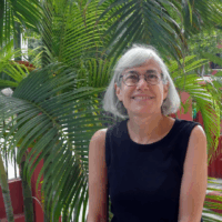 Headshot of Beth Puffer in a black sleeveless dress in front of a palm tree