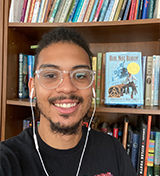 Headshot of Nick Rodriguez wearing white earbuds in front of a bookshelf