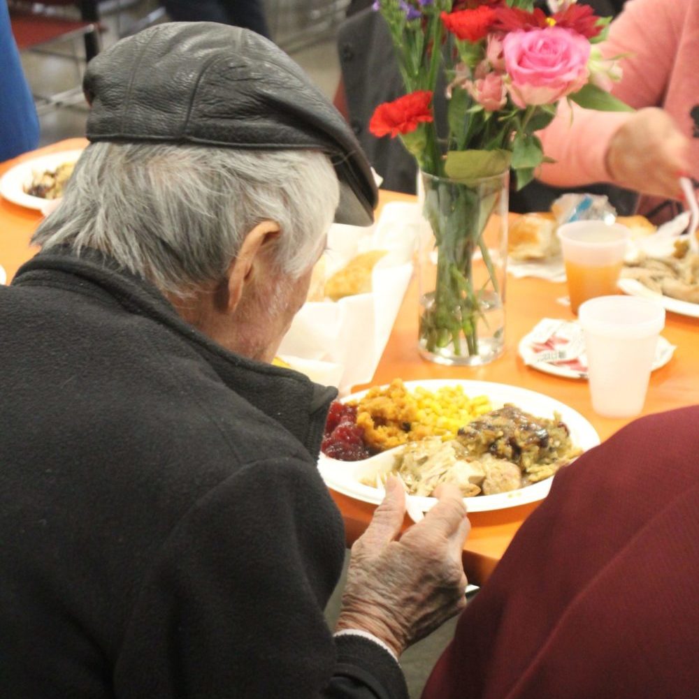 A older man facing a table eating a dinner at Goddard's Holiday Meals Thanksgiving Dinner.