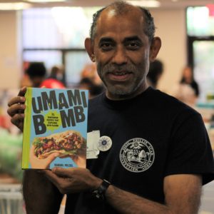 A man holding up a copy of the cookbook Umami Bomb