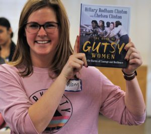 A woman holding up a copy of Hillary and Chelsea Clinton's book, Gutsy Women