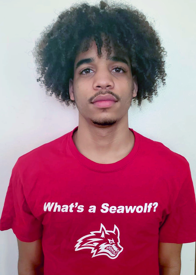 A young man wearing a red SUNY Stonybrook shirt with the slogan "What's a Seawolf?"