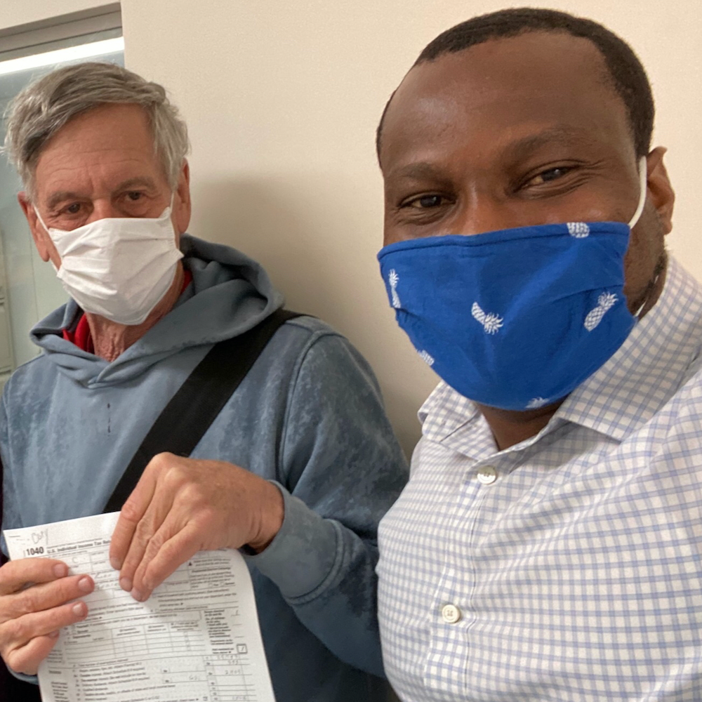 Sheldon Barasch, holding tax papers, stands next to Bobby Idowu. Both are smiling under their masks.