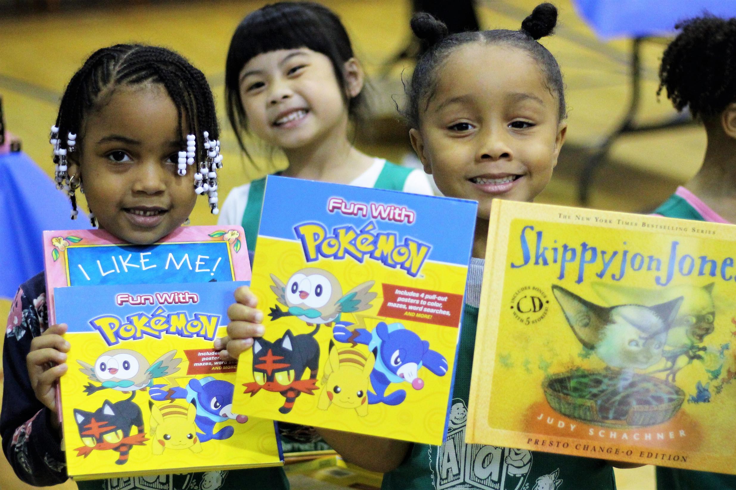 Three little girls holding picture books and smiling.