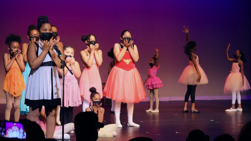 A group of young girls standing together on a stage performing a song and dance.