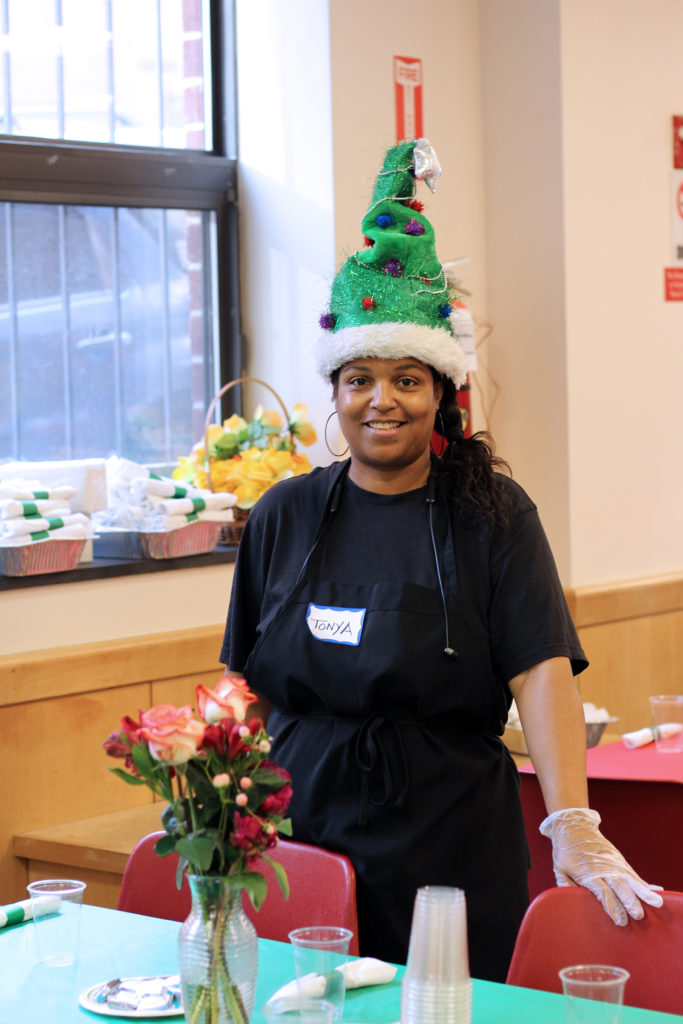 A woman standing by a table wearing a christmas hat.