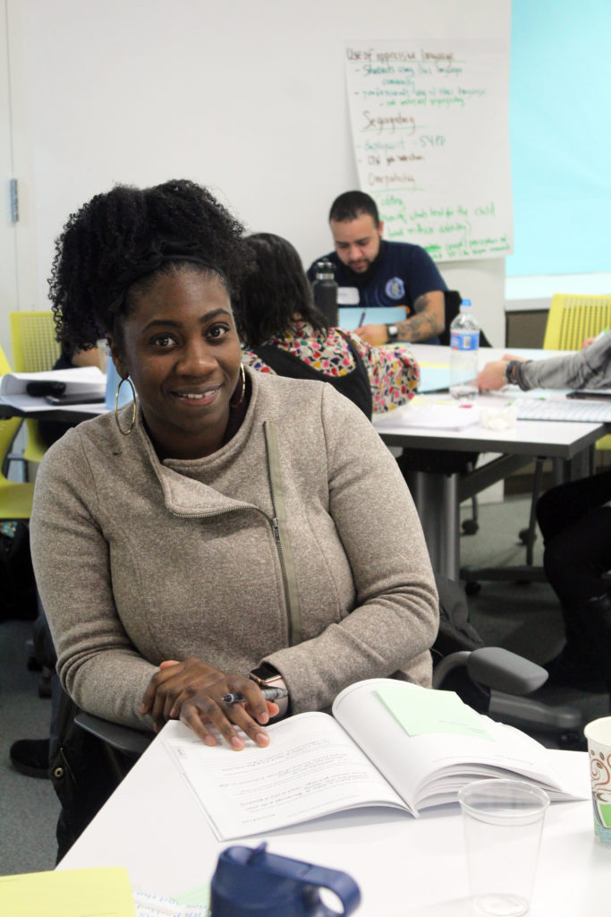 A young black woman at a Options Institute training. She is smiling with her Options Institute textbook open in front of her.