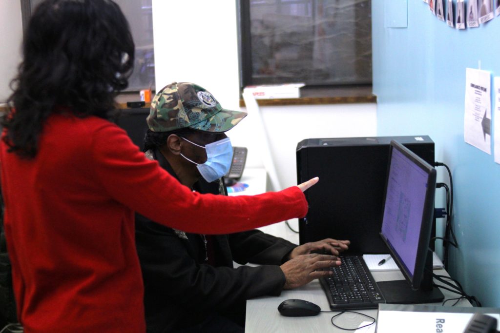A man typing on a computer with a woman giving him directions.