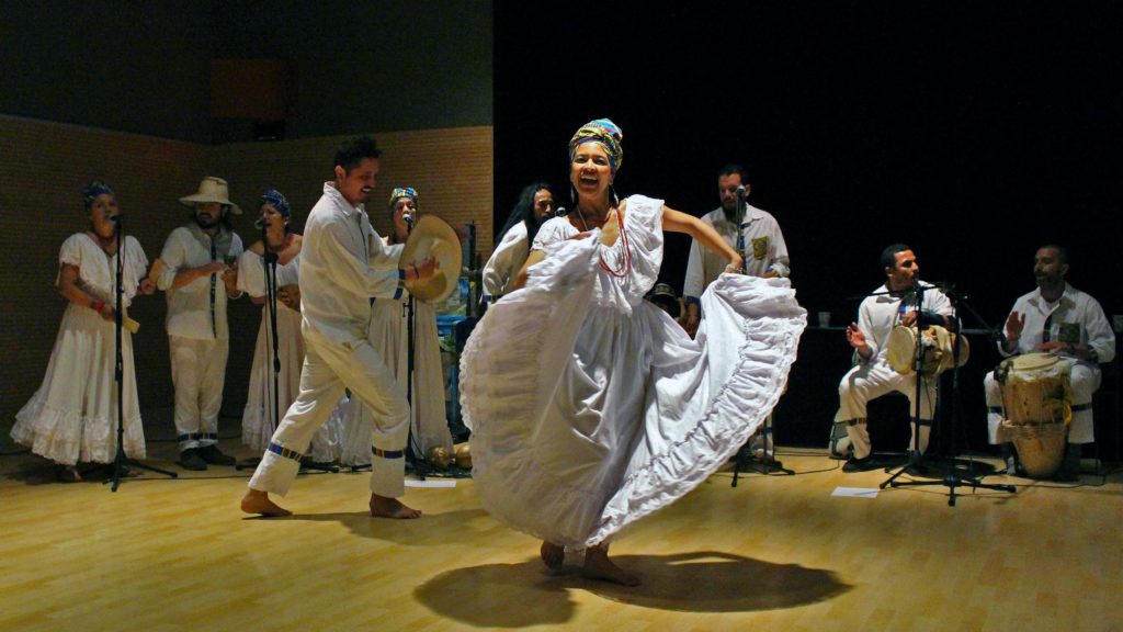 Women in a white dress dancing in front of a group singing. 