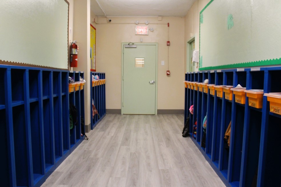 Narrow dark blue cubicles with an orange bin on their top shelf line a hallway