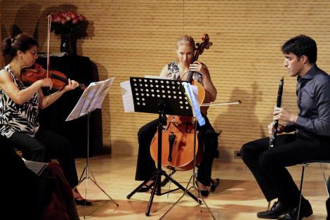 2 women playing violins and a male playing a flute.  
