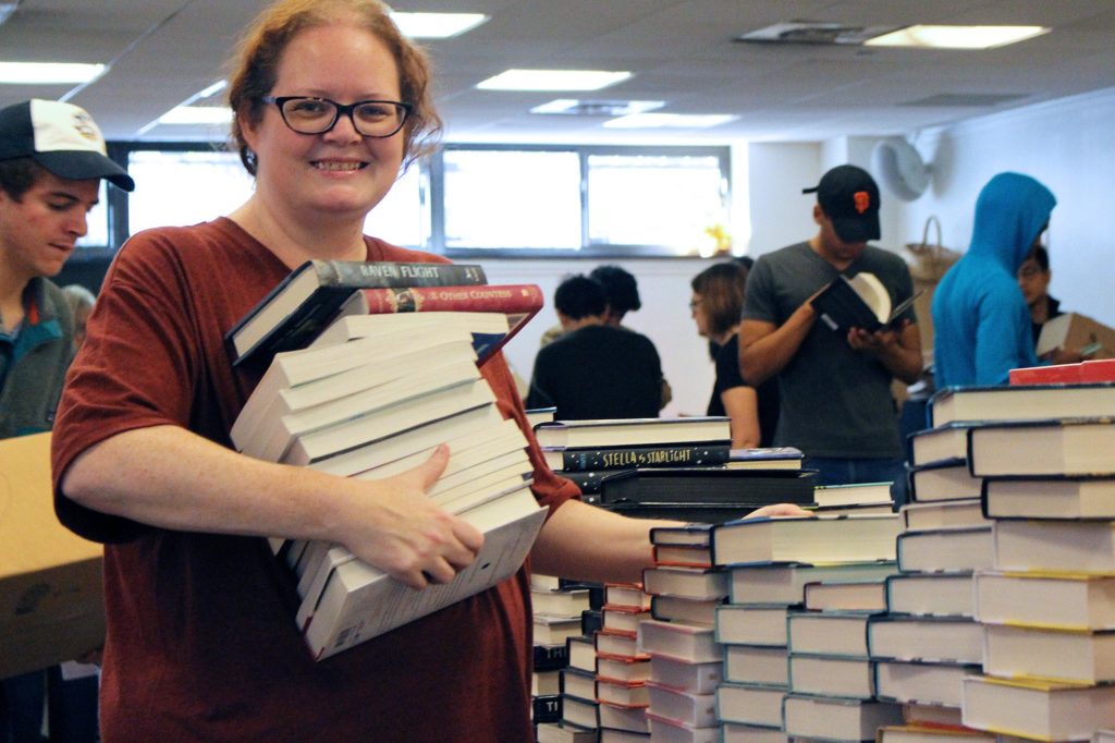 Heather Doss holding a pile of books smiling. 