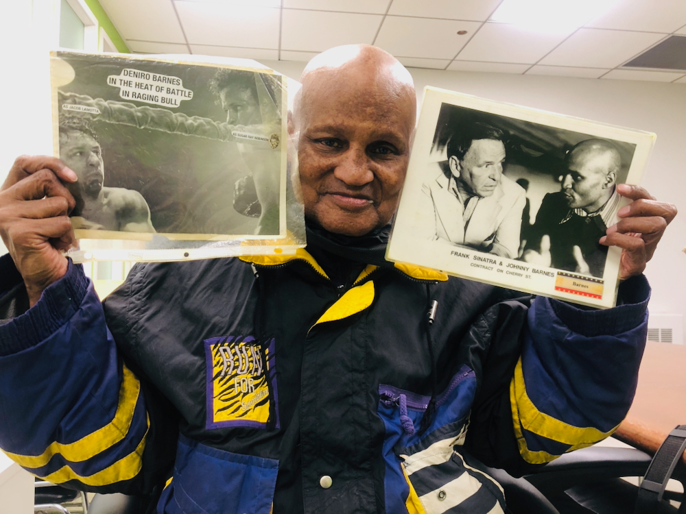 Johnny Barnes holds up two laminated photos of his biggest screen roles