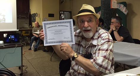 Older male holding up a certificate with a shocked face. 