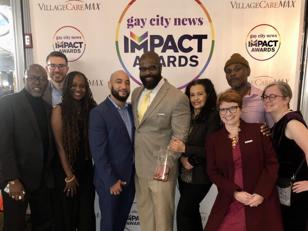 Several people pose in front of a Gay City News Impact Awards backdrop