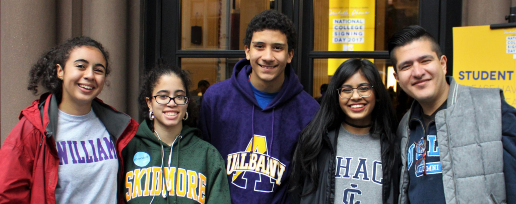 A group photo of newly accepted college students from the Options program. Wearing college sweatshirts and smiling.