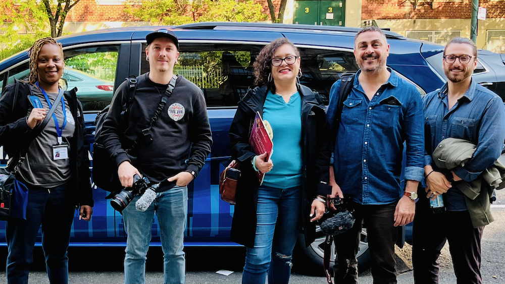 Five people, some with video gear, pose in front of an outreach vehicle