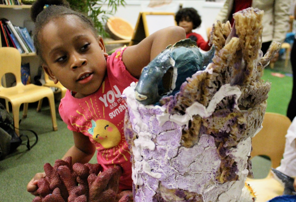 A young girl actively investigates a sculpture of a coral reef