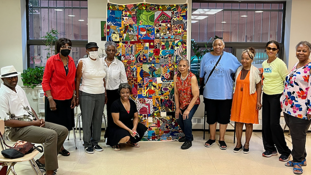 Several people pose with a colorful, irregularly patterened quilt