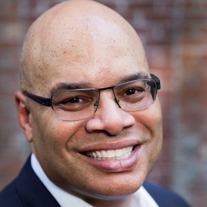 Headshot of Chris Watler smiling in a dark suit with a white shirt