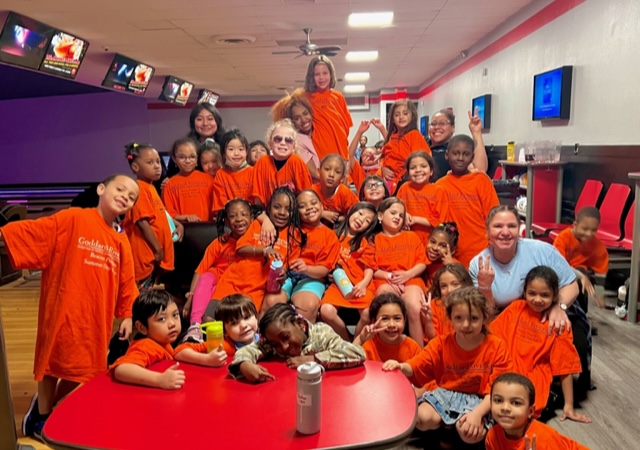 A group of children standing and smiling while on a field trip at a bowling ally.
