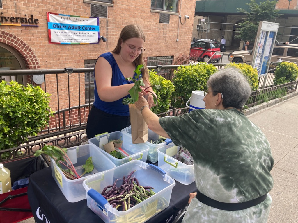Volunteer outside hands a bag of produce to a woman.