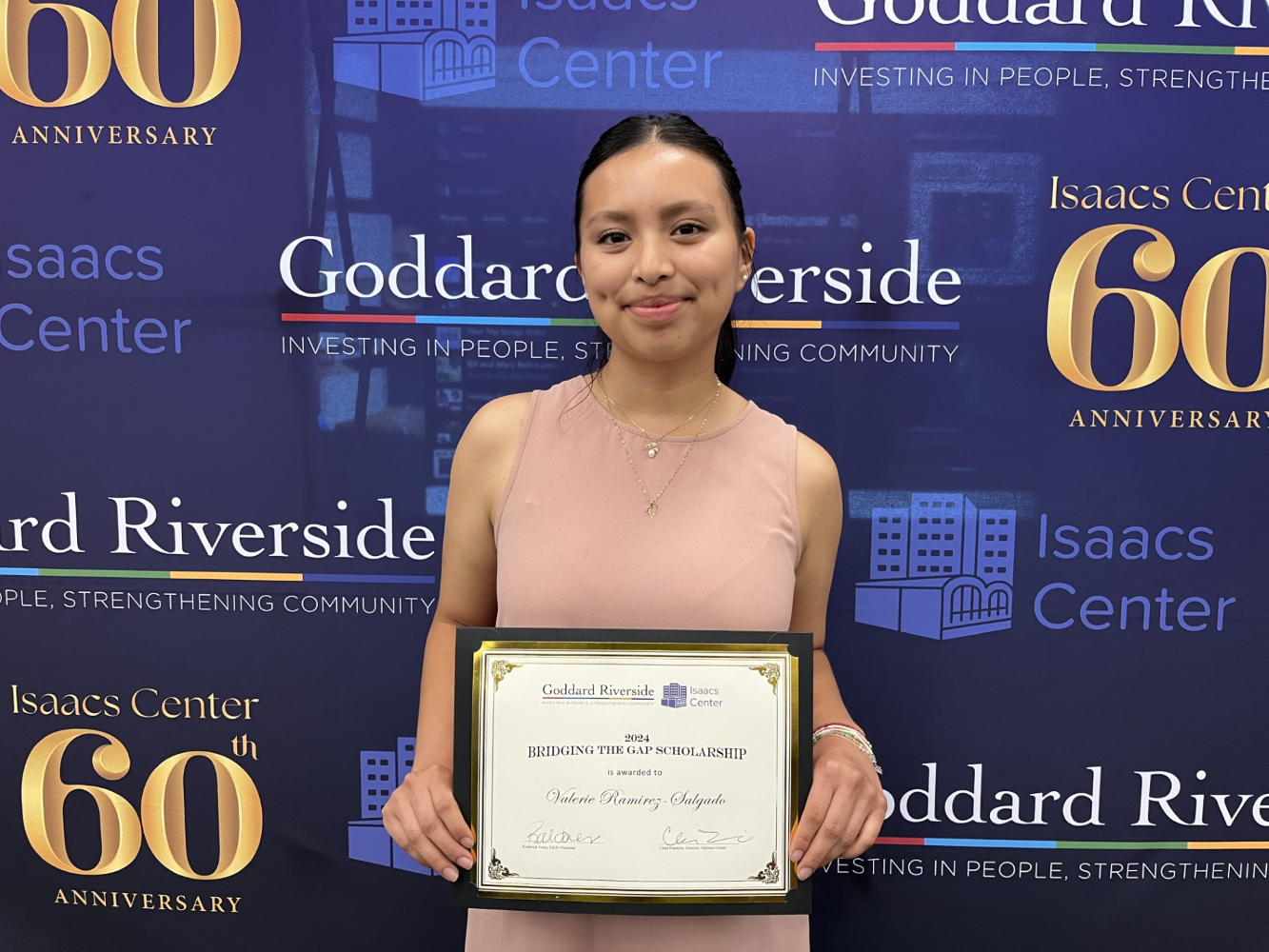 A young woman displays a scholarship certificate while standing in front of a Goddard/Isaacs Center backdrop