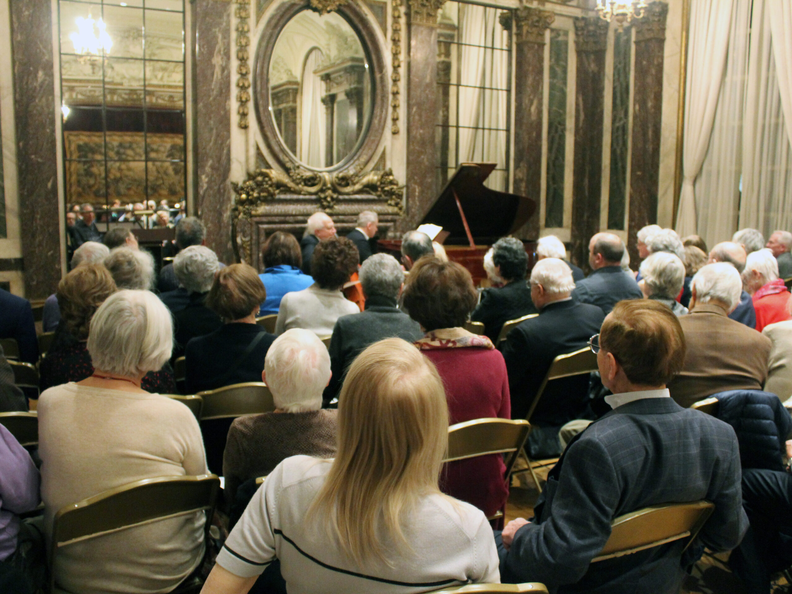 A crowd of people sitting listening to a classical music artist on a piano. 