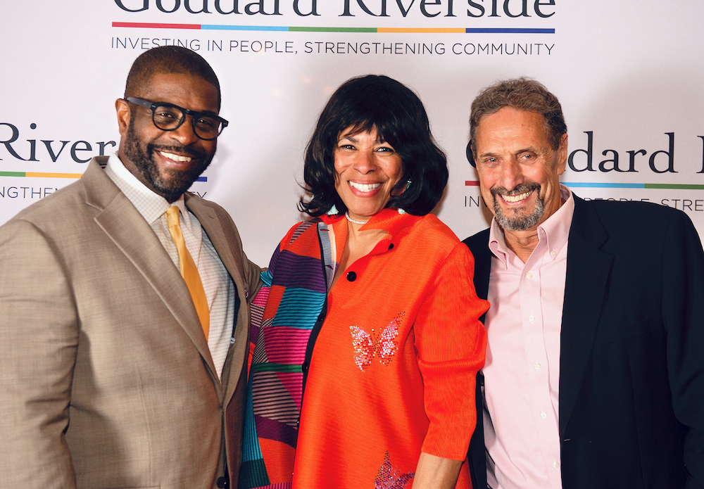 Three people pose for a photo in front of a Goddard backdrop