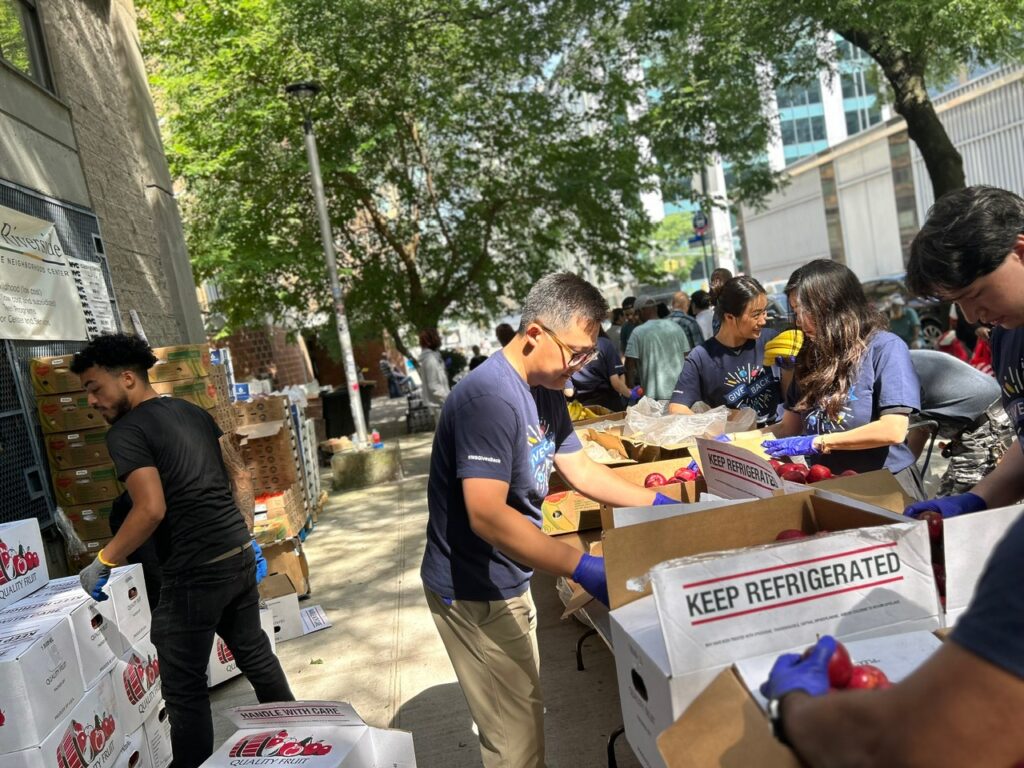 Volunteers work together outdoors, unpacking and sorting boxes of fresh produce for distribution.