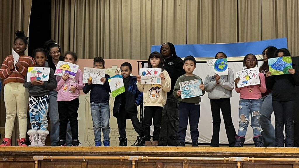 Several children stand holding pictures drawn in magic marker