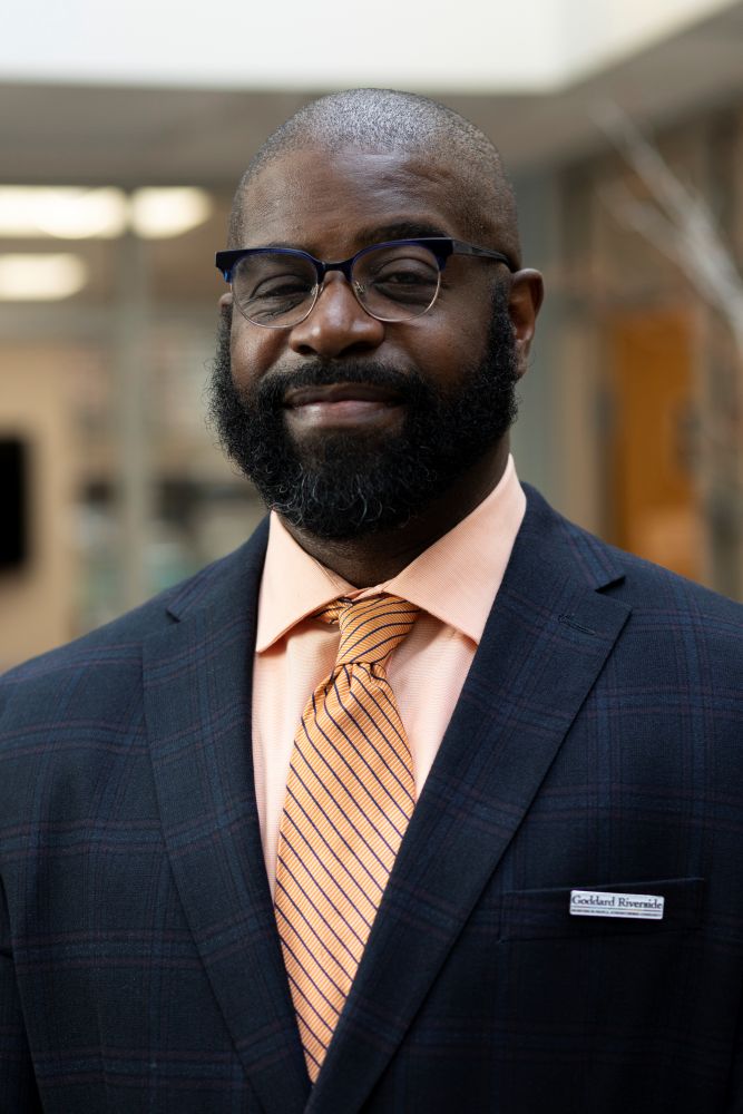 Headshot of a man in a dark suit and peach shirt and tie