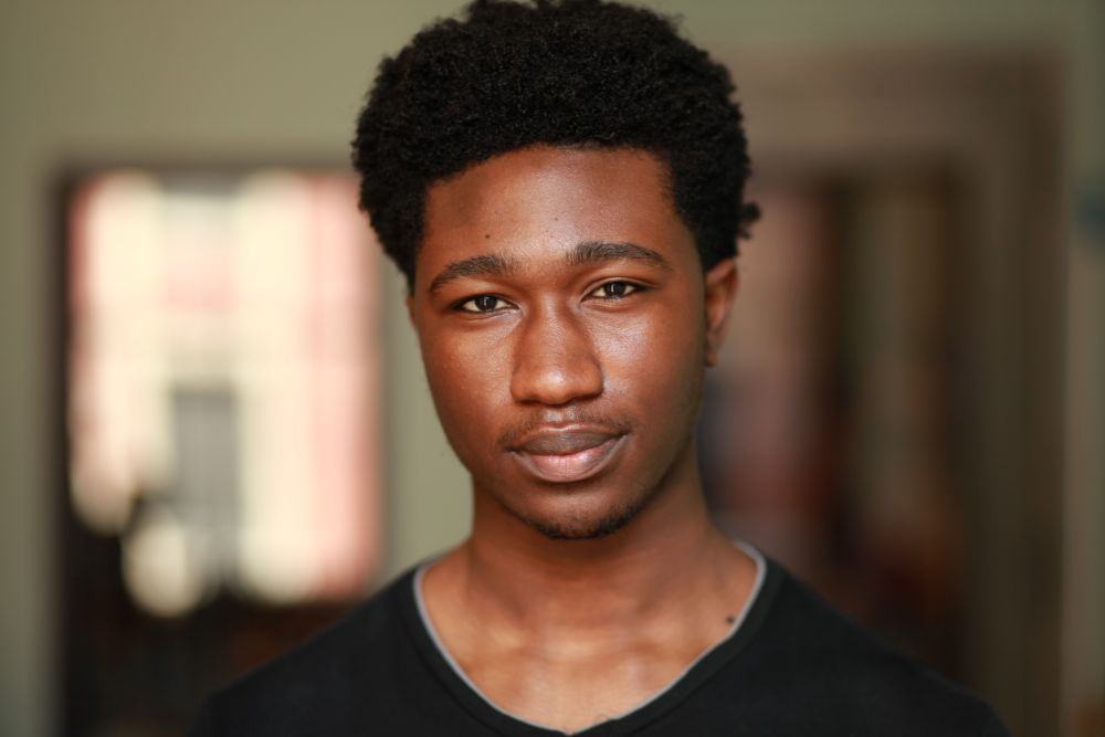 Headshot of a young black man wearing a black shirt with a warm blurred background