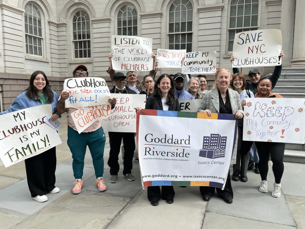 Several people stand behind a Goddard Riverside banner holding up handmade signs with slogans like My Clubhouse is my Family and Listen to the Voices of Clubhouse Members