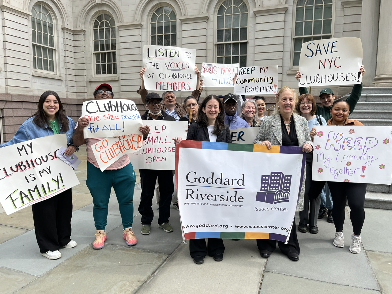 Several people stand in front of NYC City Hall with hand-made signs saying things like Save NYC Clubhouses and My Clubhouse is My Family