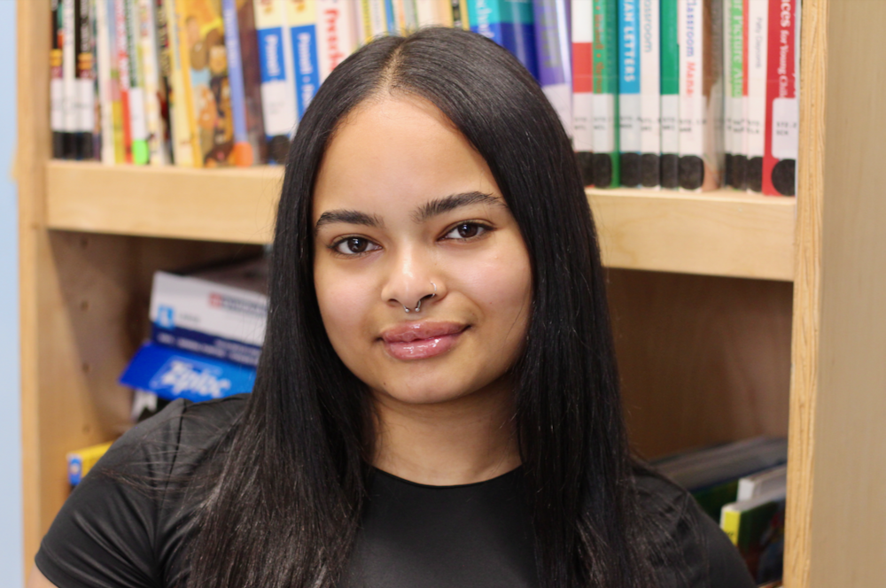A young woman poses for a photo in front of a bookcase