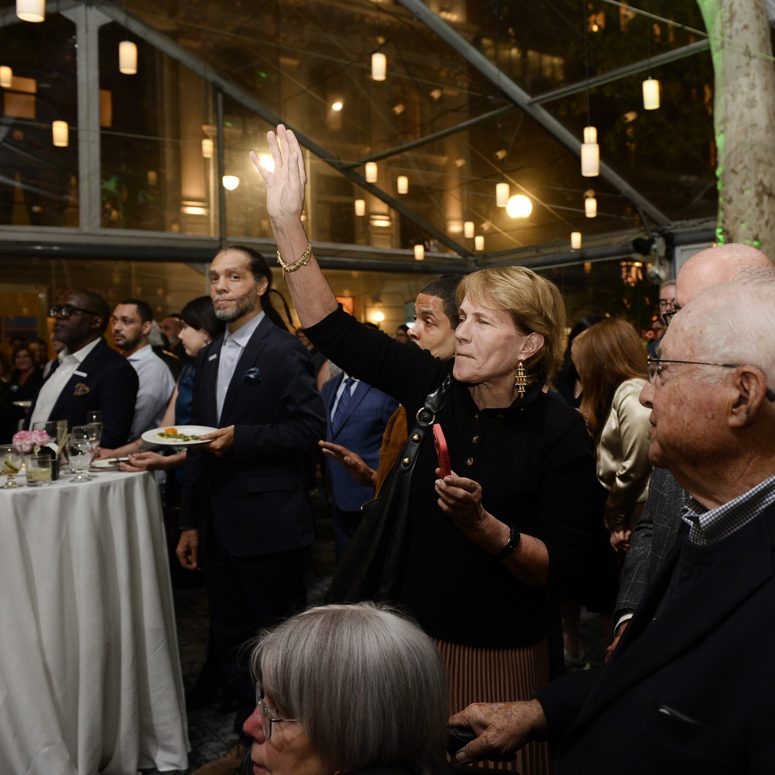 A woman in a crowd raises her hand to signal a bid