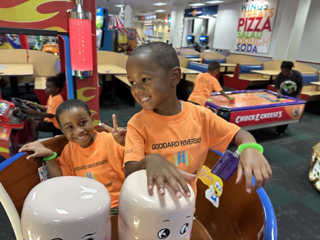 Two little boys smiling and standing together in a playroom.