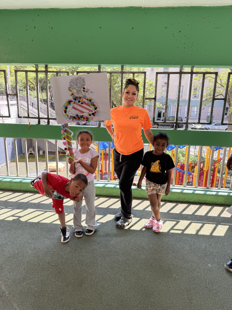A staff member standing with three campers. One child is holding a art project during summer camp.